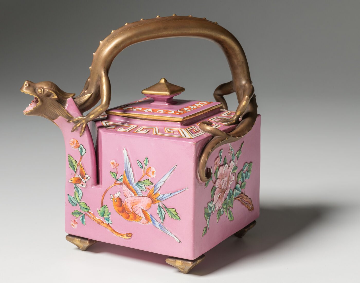 An ornate pink majolica teapot with a sculpted dragon handle