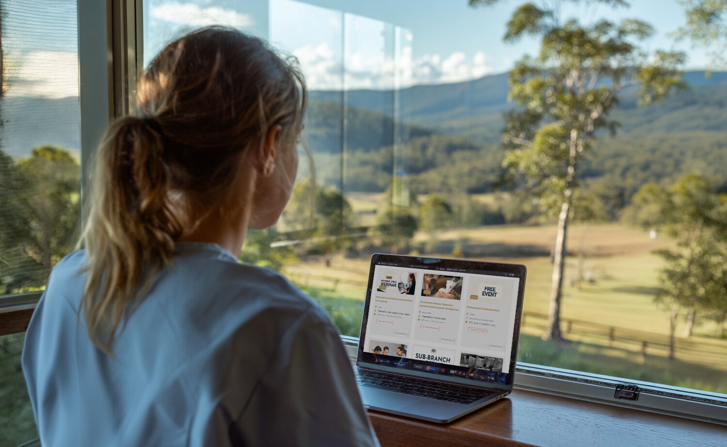 A rural practitioner at a laptop, with bushland views beyond the window